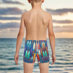 Boy wearing colorful surfboard-patterned swim shorts looking out over the Pacific Ocean in Waikiki