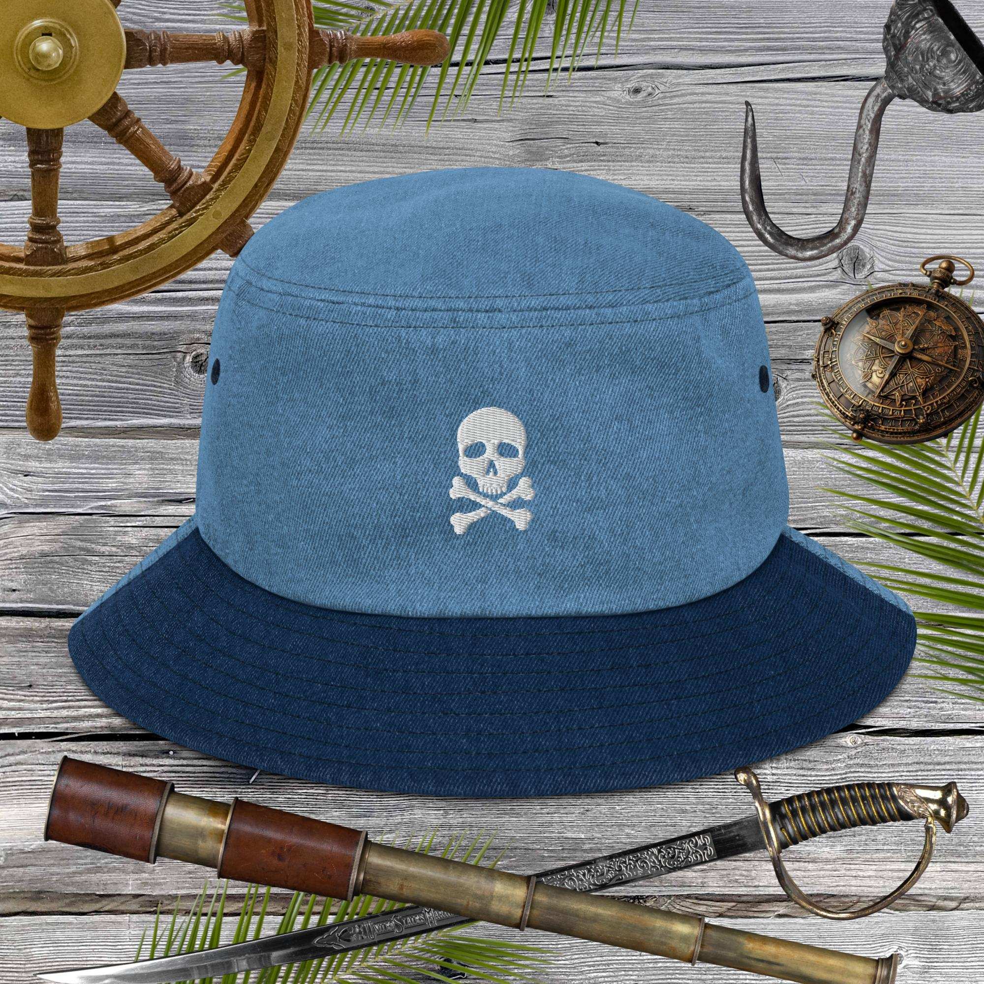 Blue bucket hat with embroidered skull and crossbones design on a wooden background with pirate-themed items.