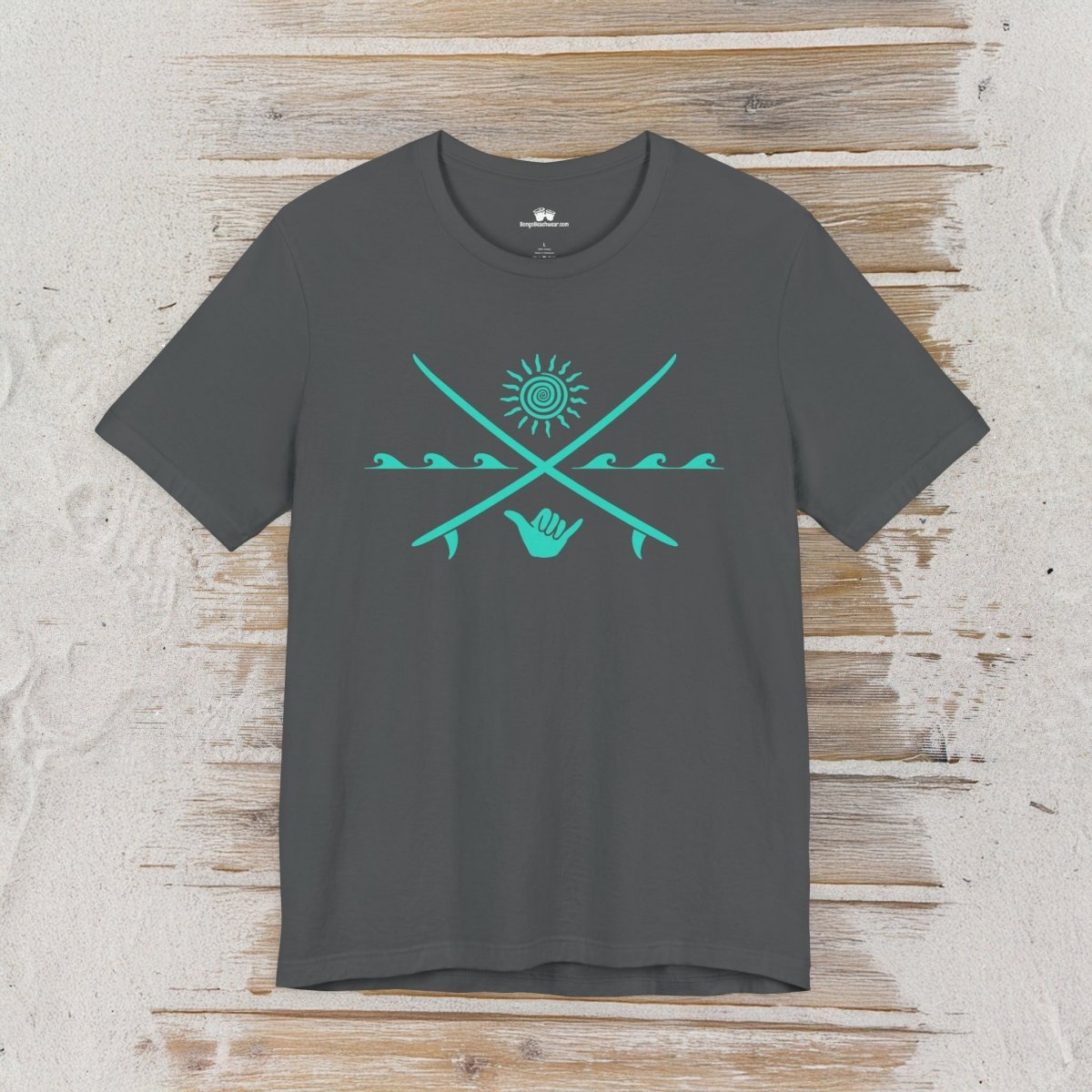 A dark charcoal gray t-shirt with a turquoise graphic of crossed surfboards, a sun, waves, and a hand gesture, displayed flat on a rustic light wood background.