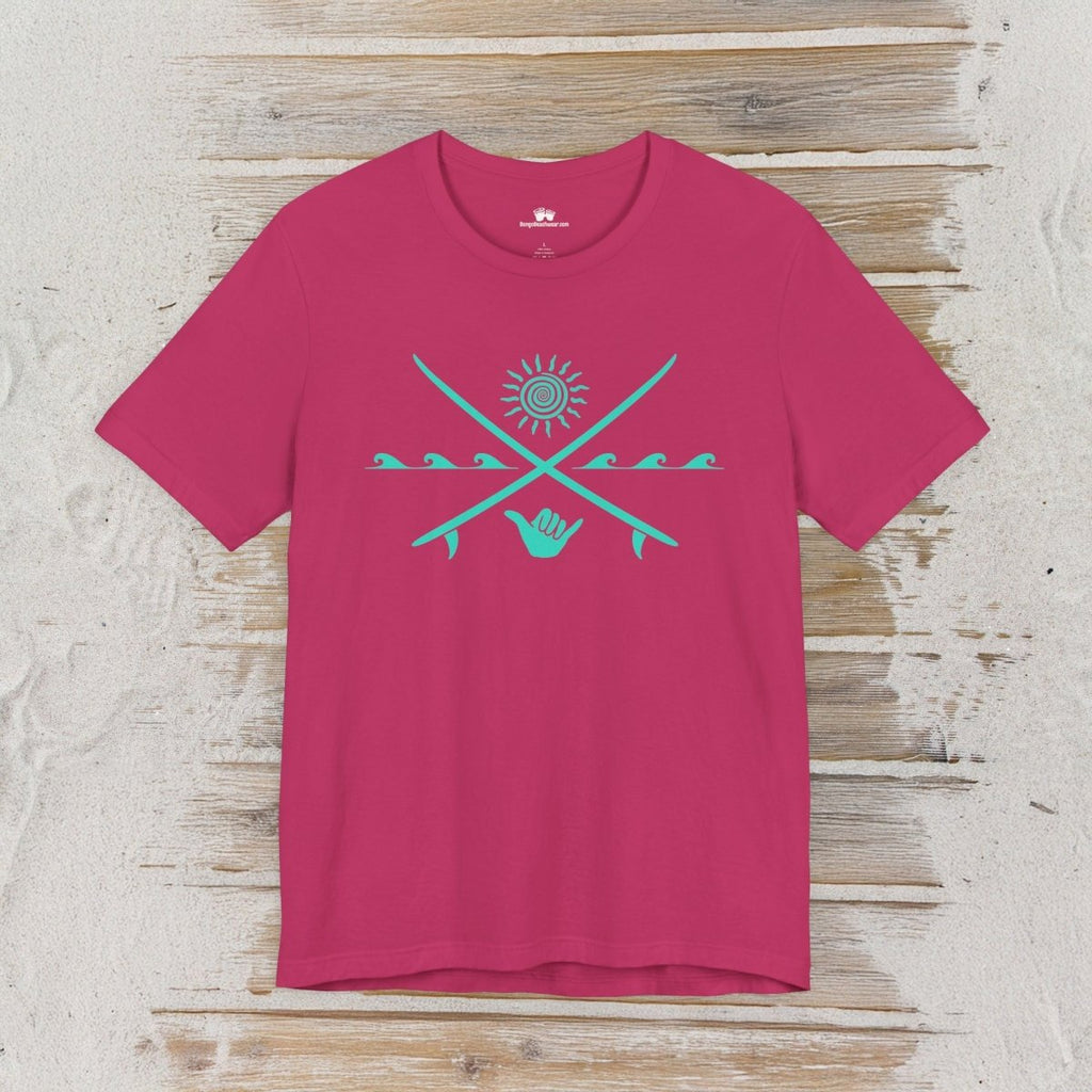 A bright pink short-sleeve t-shirt with a turquoise graphic on the chest, displayed flat against a rustic light wood background.