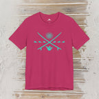 A bright pink short-sleeve t-shirt with a turquoise graphic on the chest, displayed flat against a rustic light wood background.