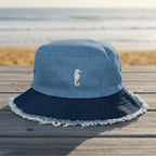 Blue bucket hat with frayed edge and a seahorse embroidery on on a beachside boardwalk
