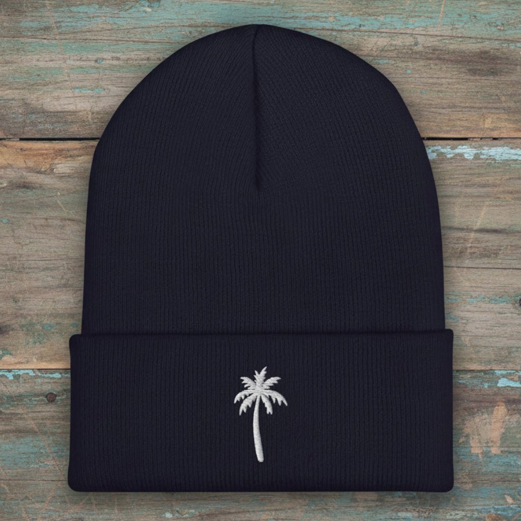 Green beanie with palm tree embroidery on a rustic wood background