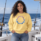 A woman with curly hair stands on a boat wearing a pale yellow sweatshirt with a colorful shark teeth graphic on the front, paired with blue jeans. Fishing rods and the ocean are visible in the background.
