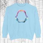 A light blue crewneck sweatshirt featuring a colorful graphic of an open shark mouth with sharp teeth on the chest, displayed against a white wood plank background with a leaf shadow overlay.