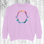 A light purple crewneck sweatshirt featuring a colorful graphic of an open mouth with sharp teeth on the chest, displayed against a white wood plank background.