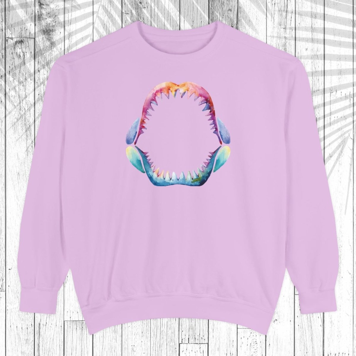 A light purple crewneck sweatshirt featuring a colorful graphic of an open mouth with sharp teeth on the chest, displayed against a white wood plank background.