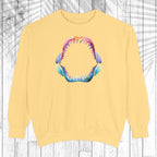 A pale yellow crewneck sweatshirt featuring a colorful graphic of an open shark mouth with sharp teeth on the chest, displayed against a white wood plank background.