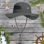 Gray shark tooth sun hat with a chin strap on a wooden background with lighthouse, steering wheel, shark teeth and palm leaves.