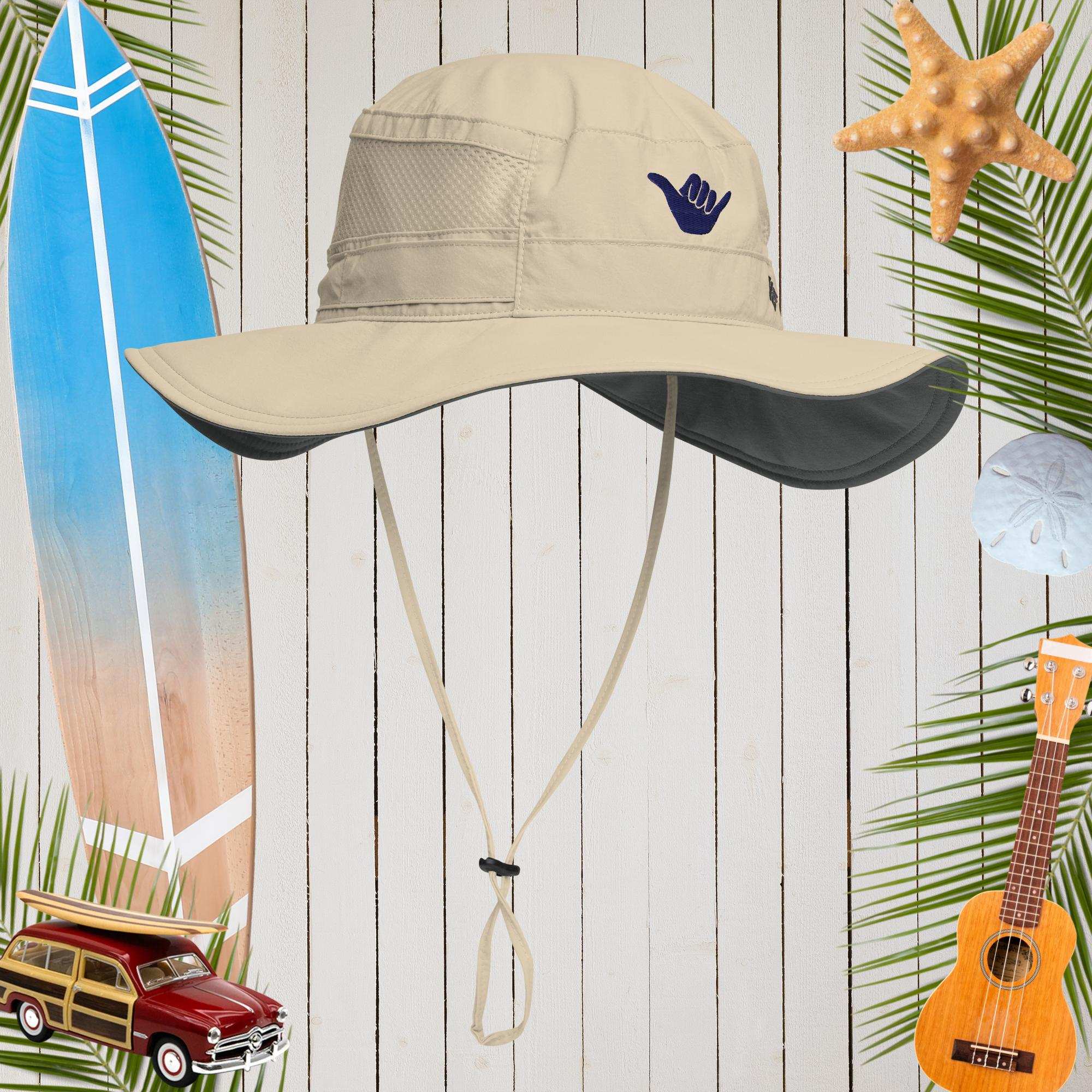 Beige sun hat with a blue shaka logo on a wooden background with beach-themed decorations.