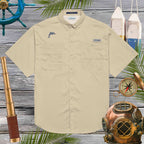 Beige shirt with an embroidered dolphin logo on a wooden background with nautical items.