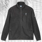 A dark gray fleece zip-up jacket with a stand collar, shown flat against a white wood plank background with a palm leaf shadow. The jacket features a small embroidered seahorse on the left chest and a small white logo on the right sleeve.