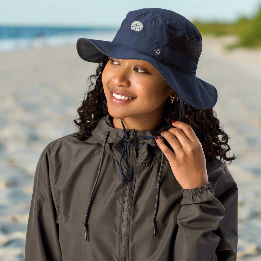 Person wearing a gray raincoat and navy bucket hat with a sand dollar embroidery standing on a beach in Long Island
