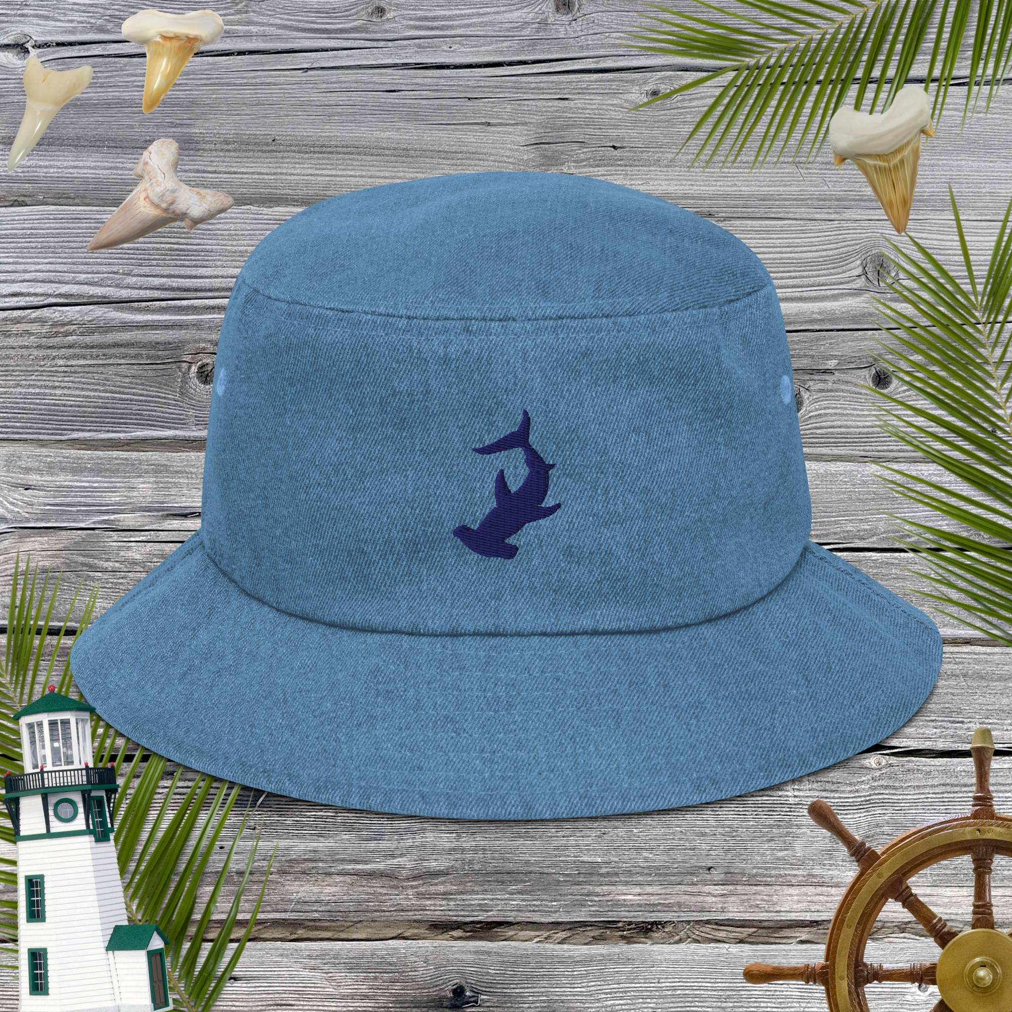 Blue denim cotton bucket hat with an embroidered shark design on a wooden background with nautical elements.