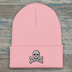A light pink ribbed knit beanie hat with a folded cuff, featuring a small embroidered gray and white skull and crossbones on the front.