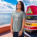 Woman wearing a t-shirt with text by a large red and white sign near water.