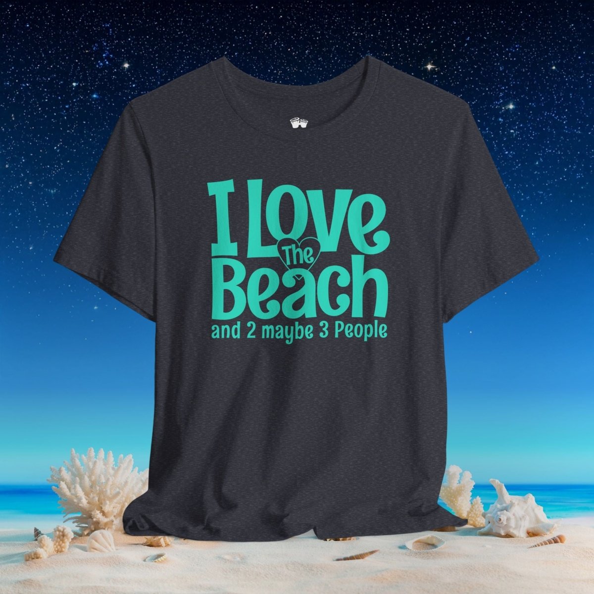 A dark charcoal gray t-shirt with a teal graphic reading 'I Love The Beach and 2 maybe 3 People' is displayed against a beach and starry night sky background.