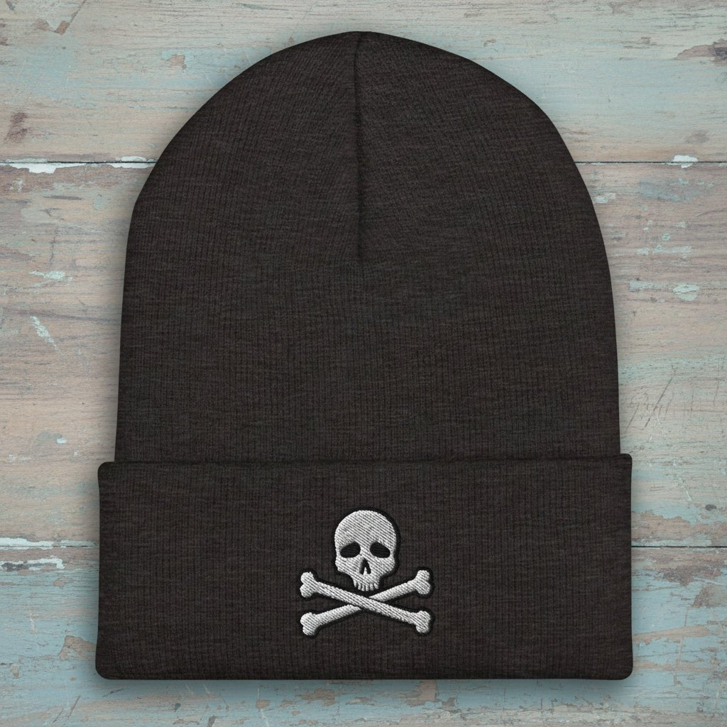A dark charcoal gray knit beanie with a folded cuff, featuring an embroidered white skull and crossbones design on the front.