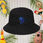 Black bucket hat with blue parrot head embroidery on a wooden background with tropical elements