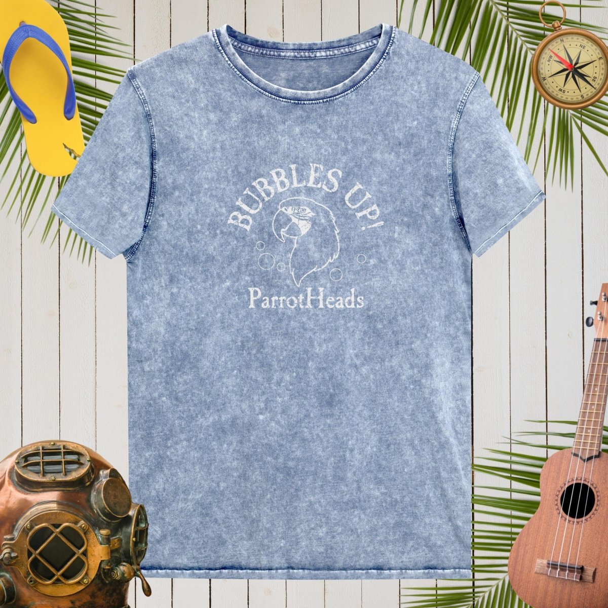 Blue t-shirt with 'Bubbles Up! ParrotHeads' design on a wooden background with tropical elements.
