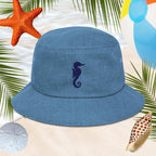 Blue bucket hat with an embroidered seahorse design on a beach-themed background with starfish, sand dollars, and shells.