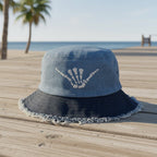 A blue denim bucket hat with a dark navy frayed brim and a white skeleton hand graphic on the front, shown against a plain white background.