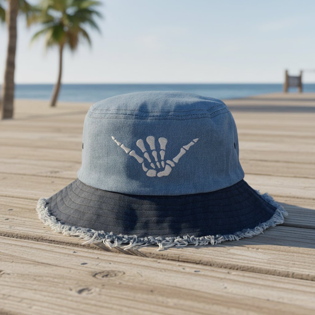 A blue denim bucket hat with a dark navy frayed brim and a white skeleton hand graphic on the front, shown against a plain white background.