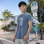 Man wearing a blue t-shirt with text standing near a scenic highway sign.