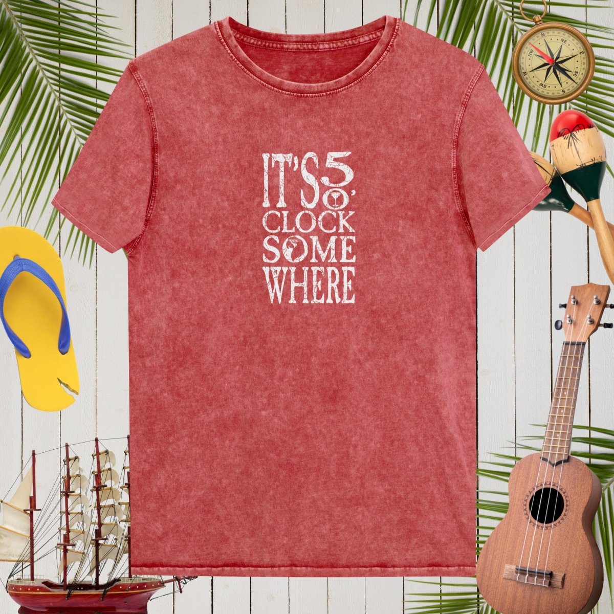 Red t-shirt with 'It's 5 o'clock somewhere' text on a wooden background with decorative items.