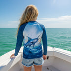 back of Tween Girl with long blond hair wearing rash guard and blue jean shorts standing on a fishing boat of the coat of Destin.