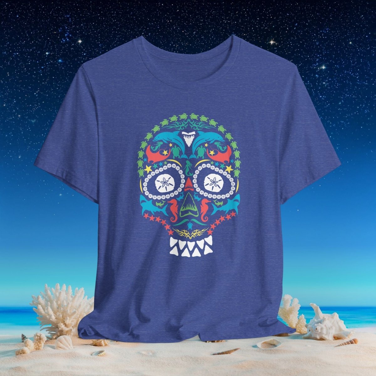 A heathered blue crewneck t-shirt featuring a colorful (sea life) Mexican sugar skull graphic on the chest, displayed on a beach background with sand, seashells, and a starry night sky.