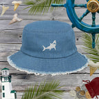 Blue bucket hat with embroidered shark design on a wooden background with nautical elements.