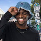 Man wearing a blue Bubbles Up Bucket Hat with a logo, smiling outdoors with scenic highway signs in the background.