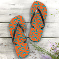Pair of orange flip-flops with teal and white dolphin pattern on a wooden surface.