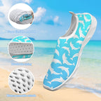 A slip-on water shoe with a blue and white dolphin pattern, shown against a beach background with three circular inset detail images highlighting its soft, breathable, and water-resistant features.