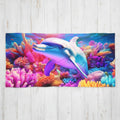 A rectangular beach towel featuring a colorful underwater scene with a blue and purple dolphin swimming among bright pink, orange, and blue coral, displayed flat against a white wood plank background.