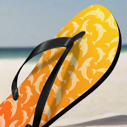 Flip-flop with dolphin pattern on a yellow and orange background sitting in the white sand of a pristine beach