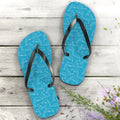 Blue flip-flops with white dolphin pattern on a wooden surface with flowers.