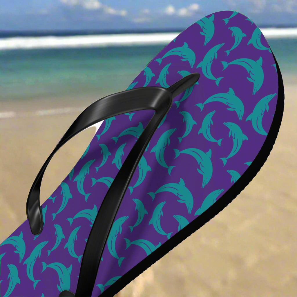 Flip-flop with purple and teal dolphin pattern on a beach background