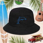 Black bucket hat with an embroidered blue dolphin design on a sandy background with surfboard, ukulele, and car.
