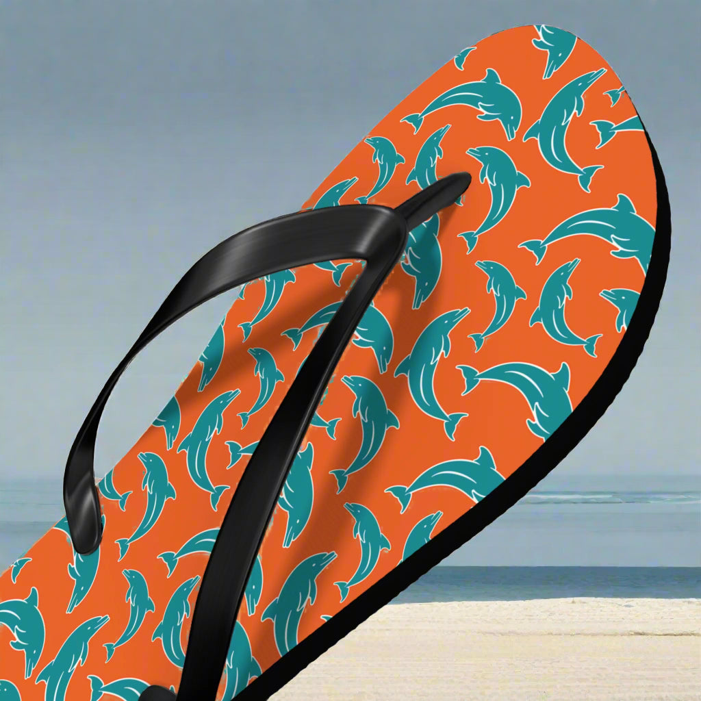 Orange Flip-flop with dolphin pattern on beach background