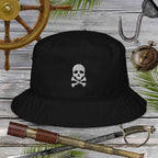 Black bucket hat with skull and crossbones design on a wooden background with pirate-themed items.
