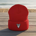 A red knit cuffed beanie hat featuring a small embroidered shark tooth logo on the front cuff, shown against a plain white background.