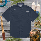 Navy blue short-sleeve shirt with embroidered dolphin logo on a wooden background with nautical-themed decor.