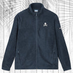 A dark navy blue fleece zip-up jacket with a small white skull and crossbones embroidered on the left chest, displayed flat against a white wood plank background with a palm leaf overlay.