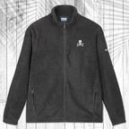 A dark gray fleece zip-up jacket with a stand collar, shown flat against a white wood plank background with a palm leaf pattern overlay. The jacket features a small white circular logo on the left chest and a small white logo on the right sleeve.