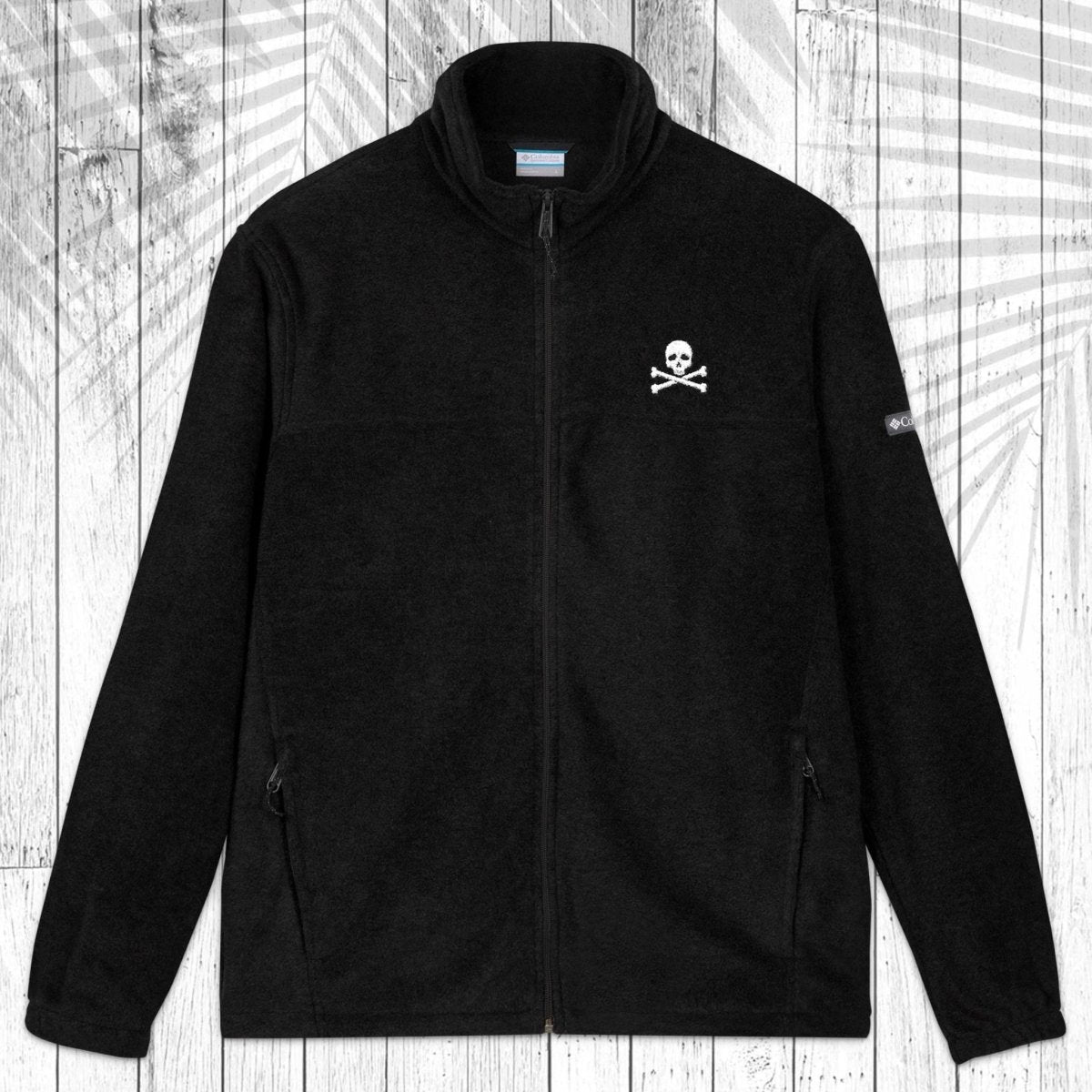 A black fleece zip-up jacket with a stand collar, shown flat against a white wood plank background with a palm leaf pattern overlay. The jacket features a small white circular logo on the left chest and a small white logo on the right sleeve.