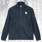 A dark navy blue fleece jacket with a full-zip front, stand-up collar, and zippered hand pockets, laid flat on a white wood plank background with a palm leaf pattern overlay.