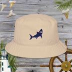 Beige bucket hat with embroidered shark design on a wooden background with nautical elements.