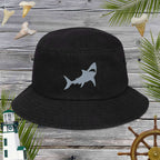 Black bucket hat with embroidered shark design on a wooden background with nautical elements.